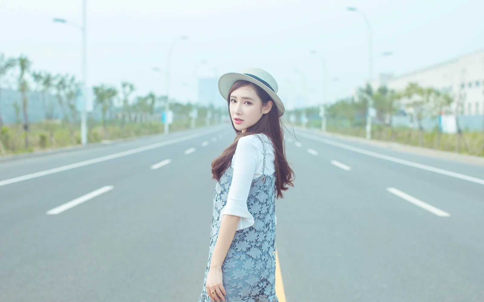 一名戴帽子的女性站在宽阔公路中央回望镜头。