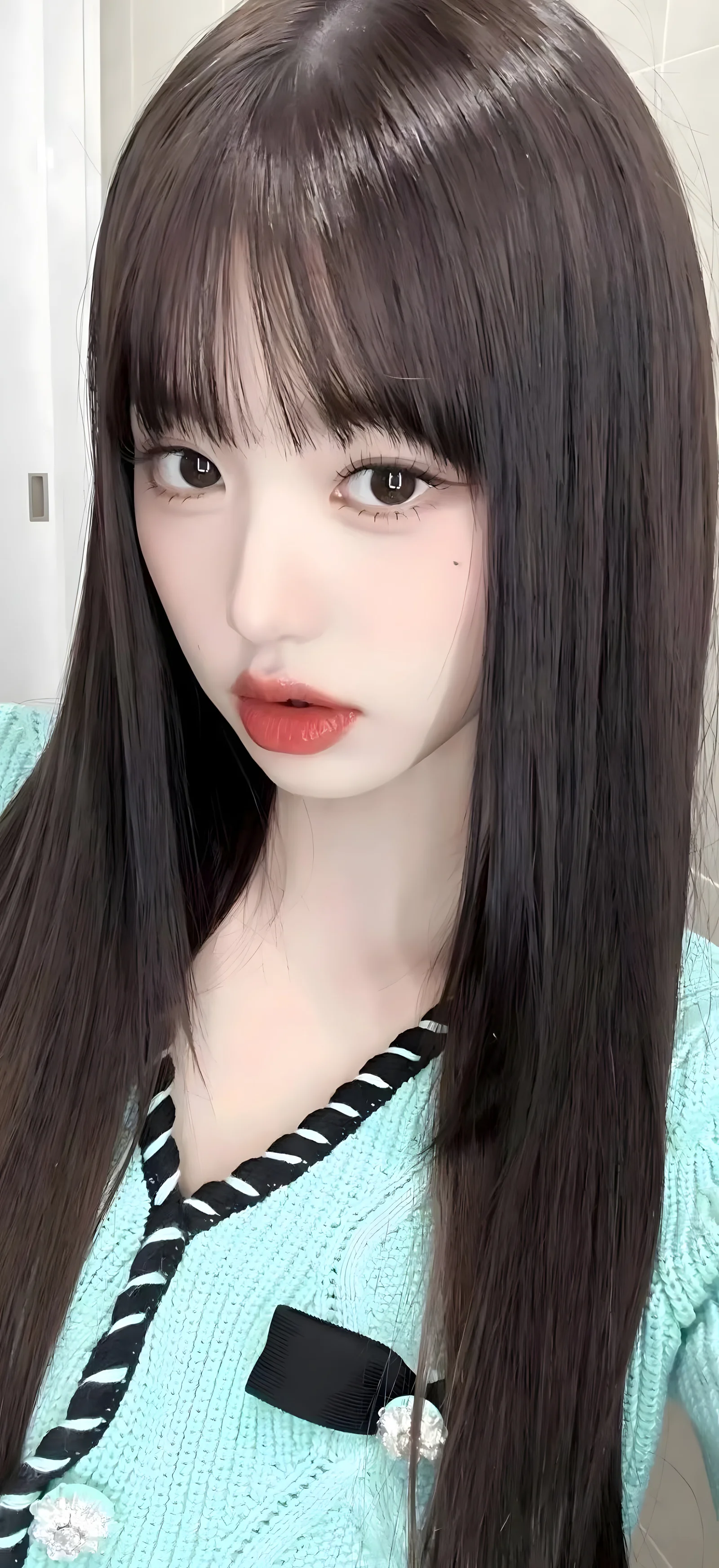 긴 머리의 여성이 연한 청록색 니트를 입고 실내에서 카메라를 바라보고 있습니다.