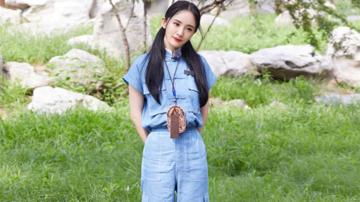 파란색 옷을 입은 여성이 푸른 풀과 바위로 둘러싸인 야외에 서 있다.