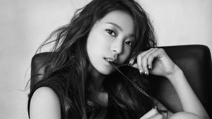 一名成年女性坐在椅子上，以黑白风格注视镜头，手持链条靠近嘴边。