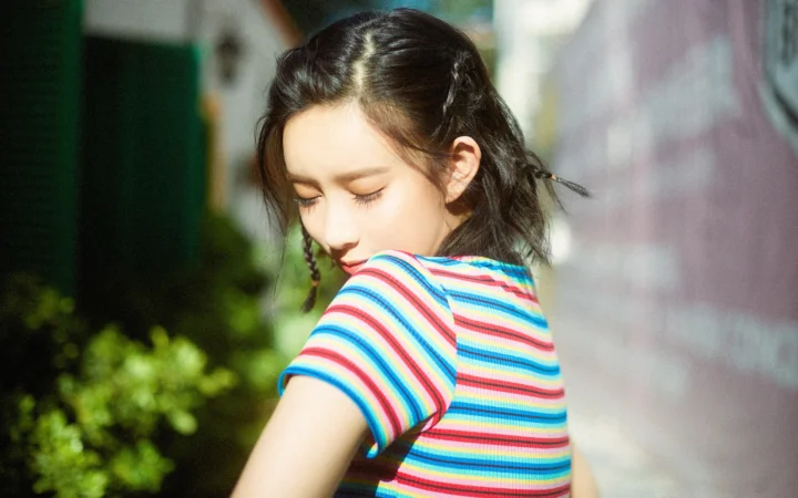 알록달록한 줄무늬 셔츠를 입은 여성이 야외 햇살 속에서 뒤돌아보고 있다.