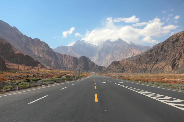 一条公路通向帕米尔高原群山之间，远处雪山耸立在蓝天白云下。