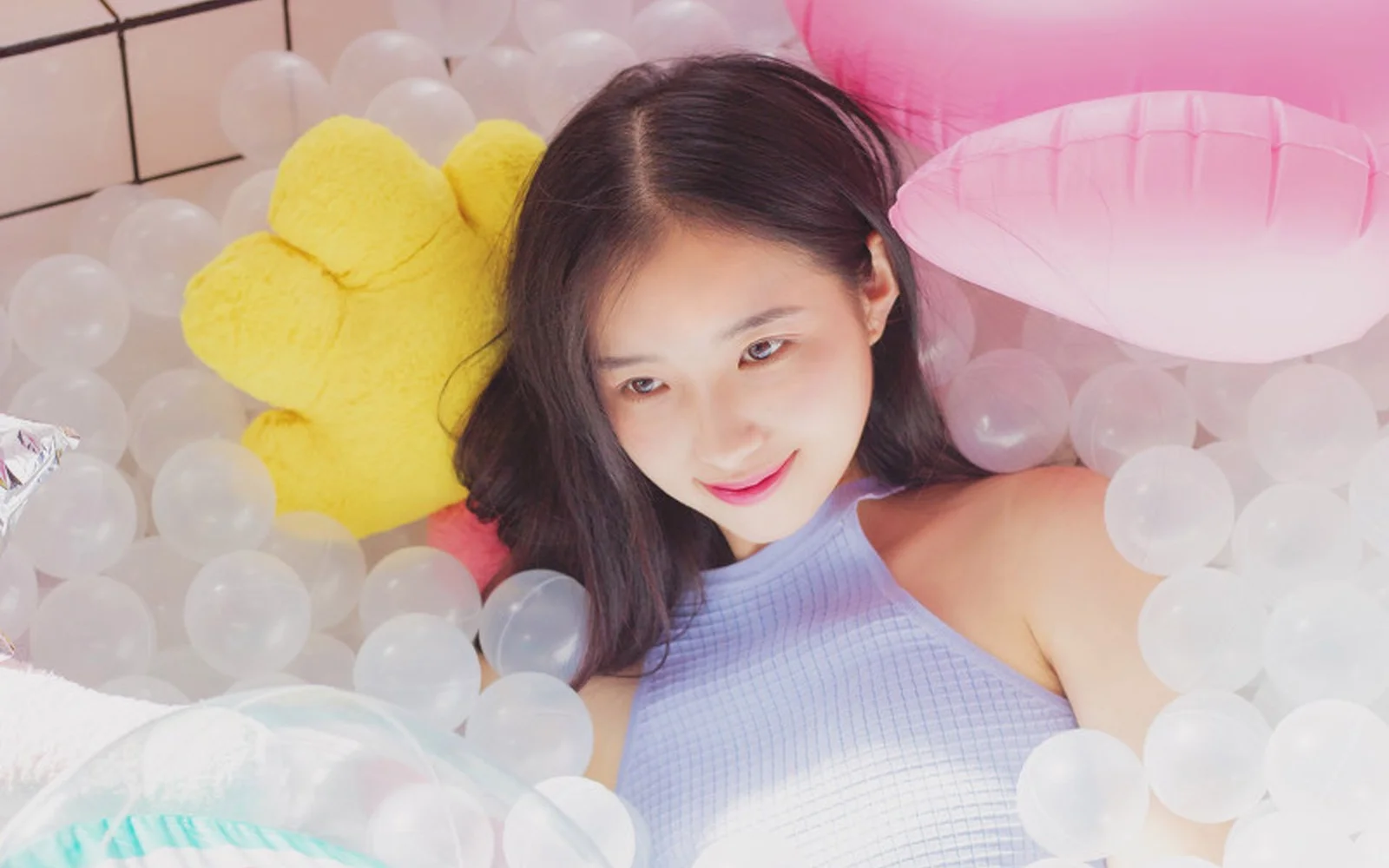 大人の女性が色とりどりの風船に囲まれて横たわっている室内の一場面です。