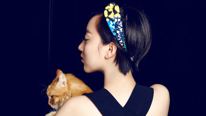 一名成年女子侧身闭眼抱着一只橘猫，背景为深蓝色。