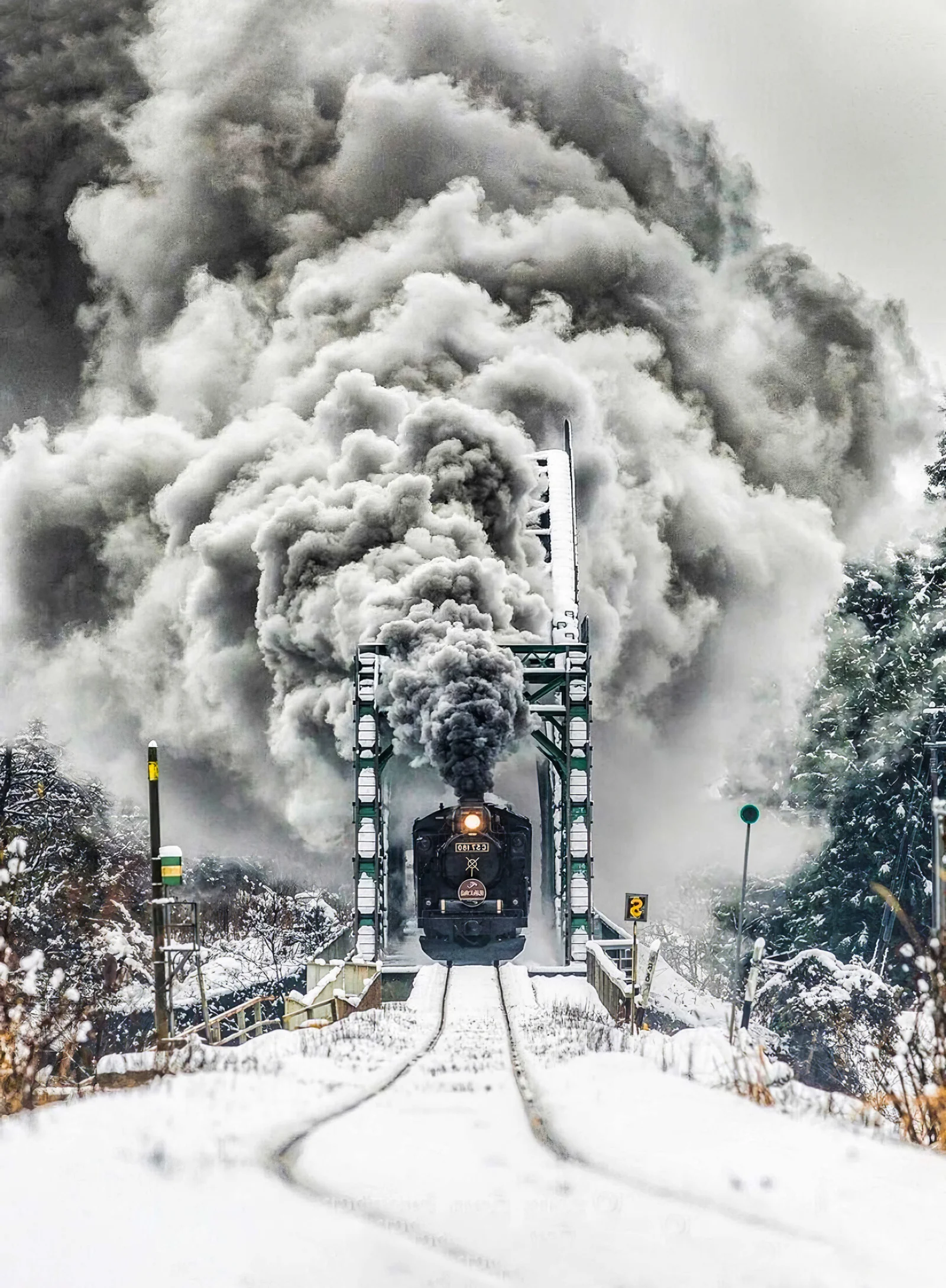 一辆蒸汽火车穿过积雪覆盖的铁路桥，浓烟在上方翻涌。