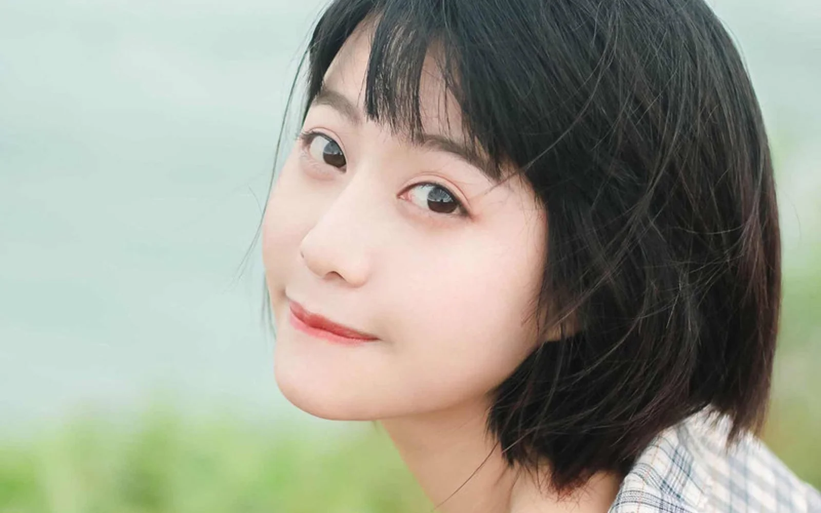 짧은 머리의 여성이 부드러운 연녹색 야외 배경 앞에서 카메라를 바라보는 클로즈업 인물 사진입니다.