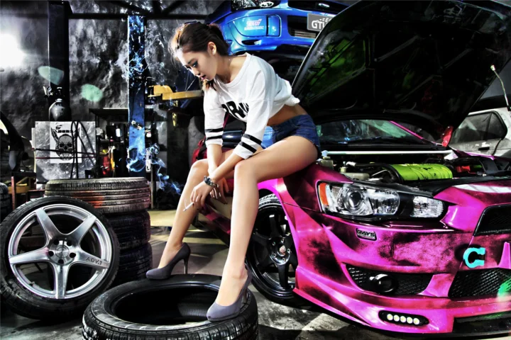 一名成年女性坐在车库内一辆亮粉色跑车旁，周围可见其他汽车、轮胎和轮毂。