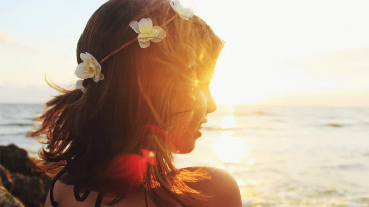 一位戴着花环的女性在海边夕阳下侧身望向海面。