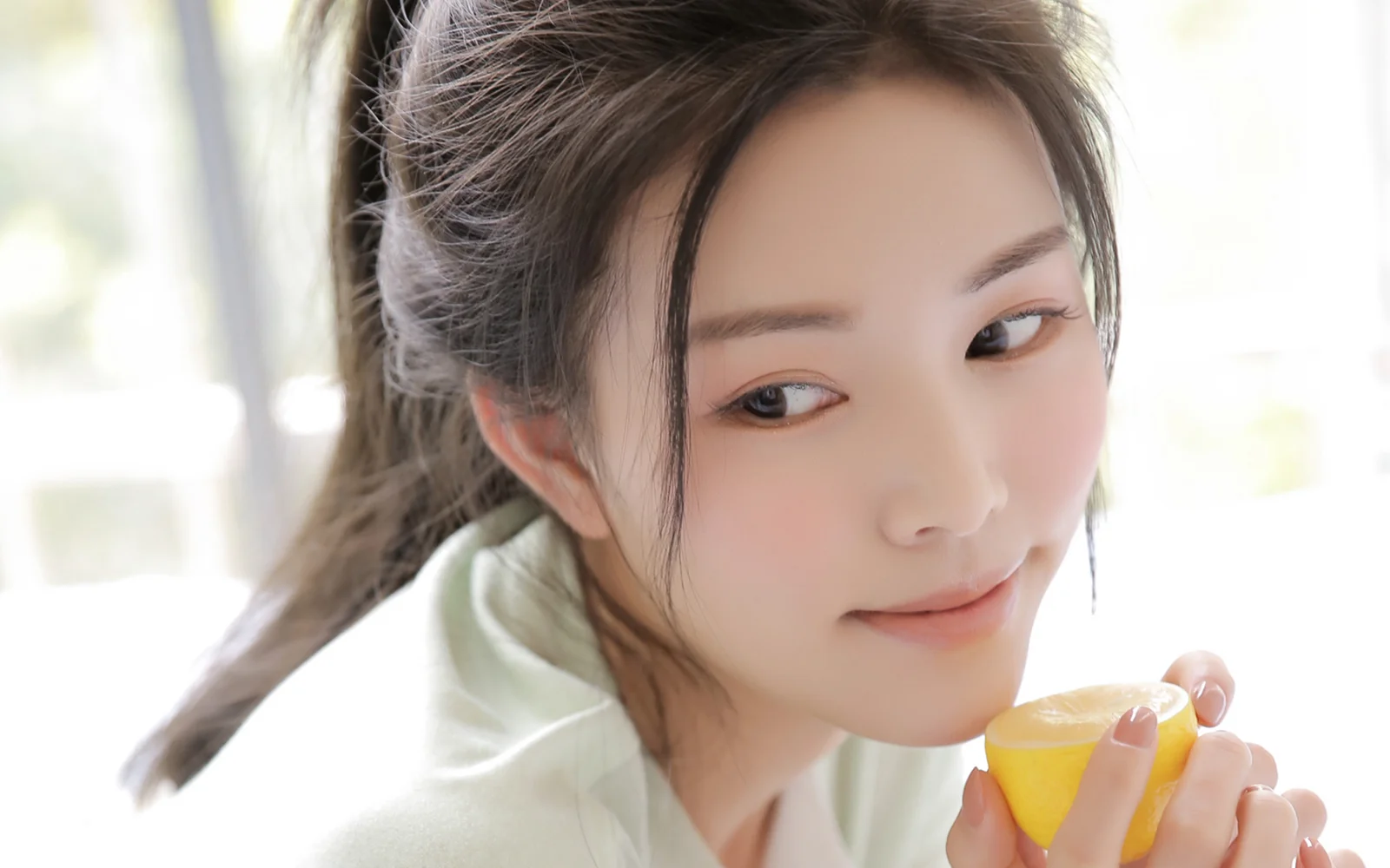 明るく柔らかな光の中で、黄色い柑橘類を手にした成人女性を写したクローズアップポートレートです。