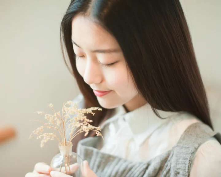 긴 머리의 여성이 눈을 감고 드라이플라워를 들고 있는 부드럽고 밝은 인물 사진입니다.