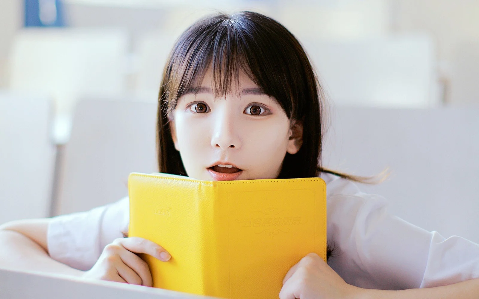一名女子在明亮室内手持黄色书本面对镜头。