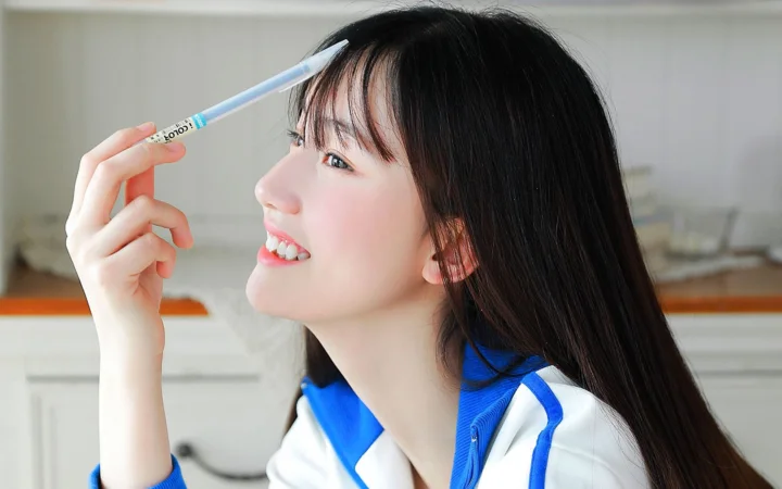 一名长发女子微笑着举起一支笔，画面呈现蓝白色服装和明亮的室内背景。