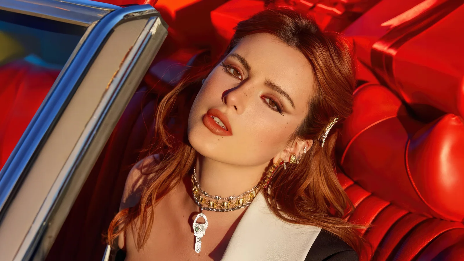 빨간 자동차 시트 옆에서 목걸이를 착용한 성인 여성이 카메라를 바라보고 있다.