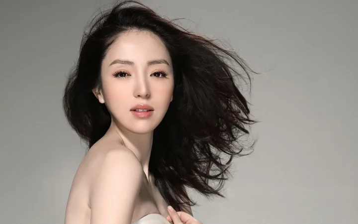 一名黑发女性在灰色背景前面对镜头，长发向一侧飘散。