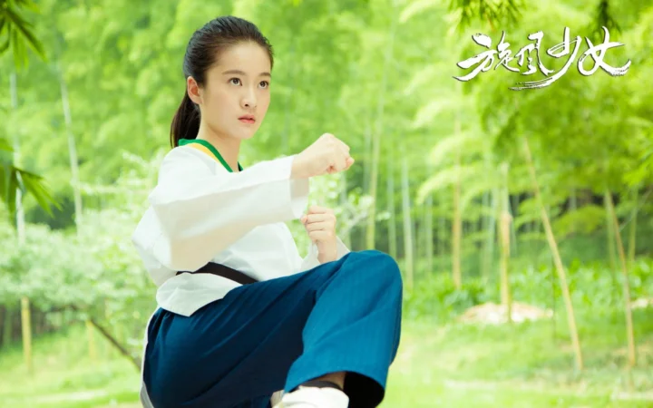 一名身穿白色上衣和蓝色裤子的女子在竹林中摆出武术姿势。
