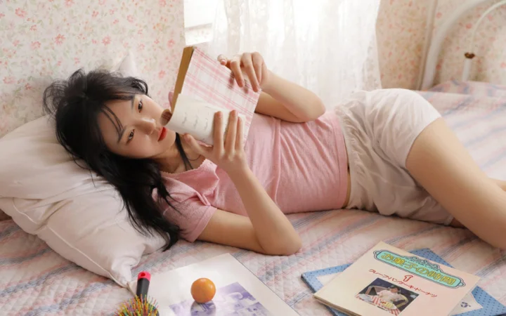 一名女性躺在床上阅读，周围是柔和的粉色室内装饰。