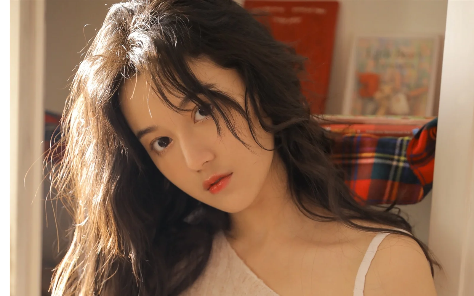 一位长发女性在室内阳光下侧头注视镜头。