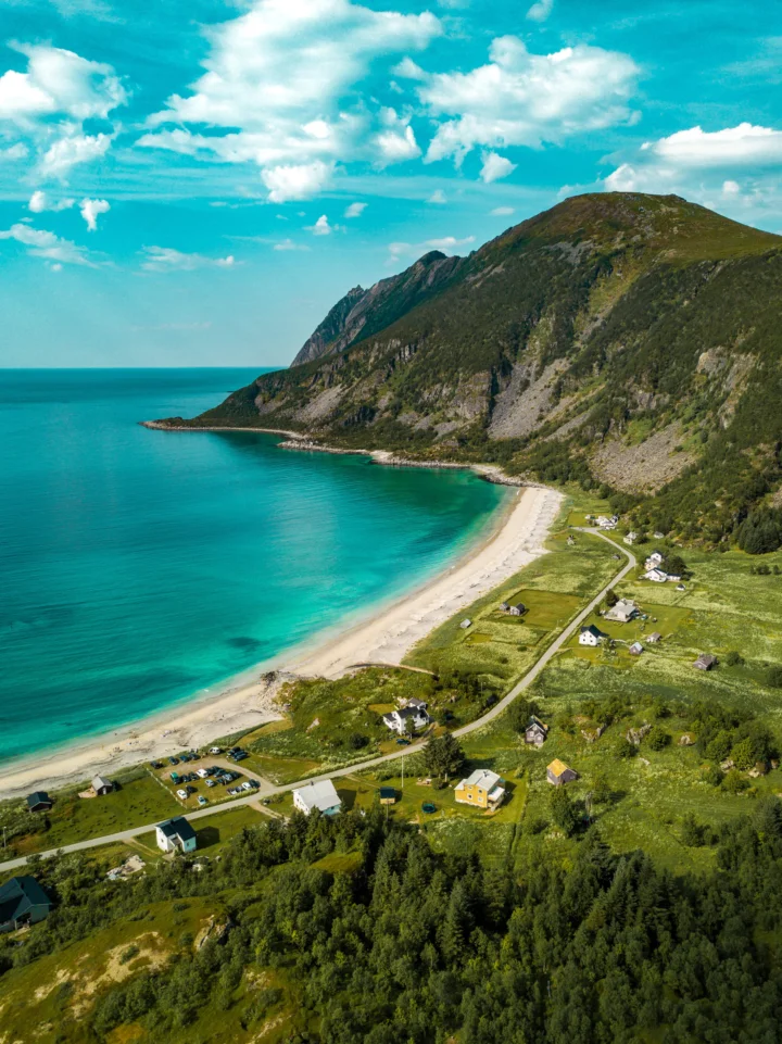 碧蓝海湾、沙滩、山脉与沿海村庄构成一幅明亮的航拍风景。