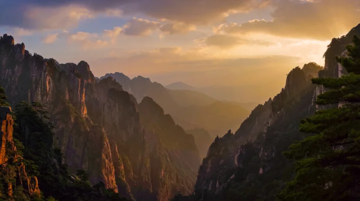 夕阳照亮群山峡谷，远处山峰笼罩在雾霭之中。