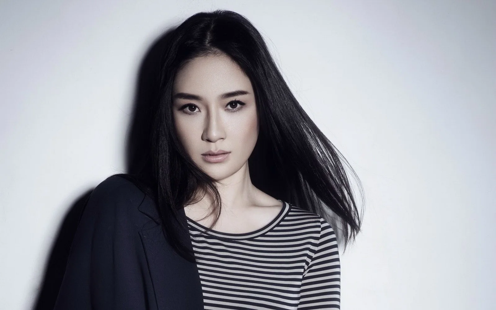 검은 머리의 여성이 검은색과 흰색 줄무늬 상의를 입고 밝은 회색 배경 앞에 서 있습니다.