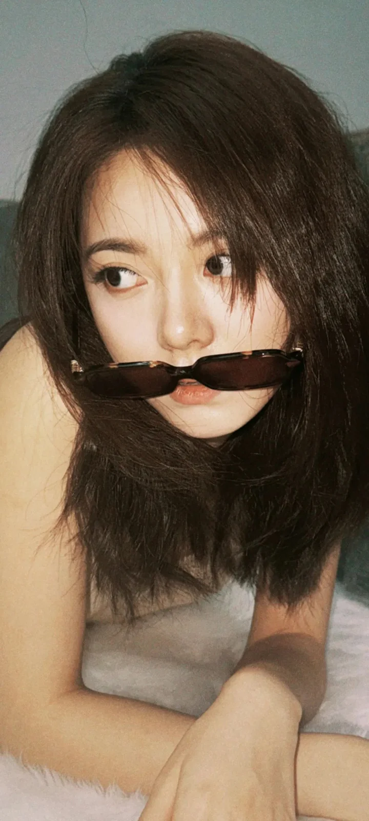 一名长发女性戴着墨镜，靠近镜头坐在室内。