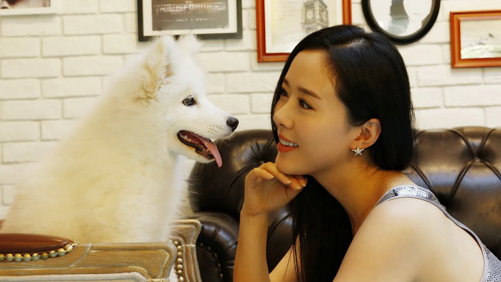 一名成年女性在室内沙发旁与一只白色狗狗相视而望。