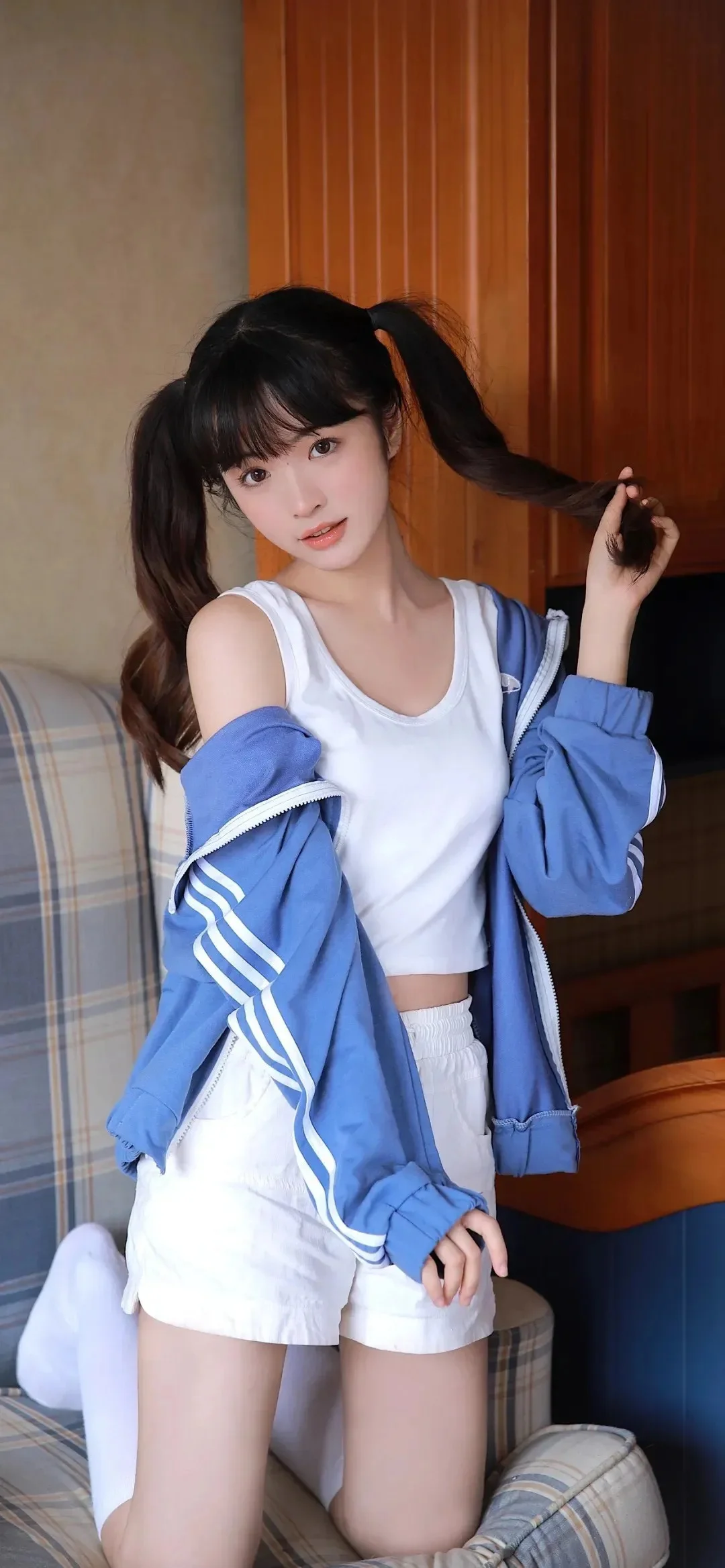 長い髪の女性が青いジャケットと白い服を着て室内の椅子に座っています。