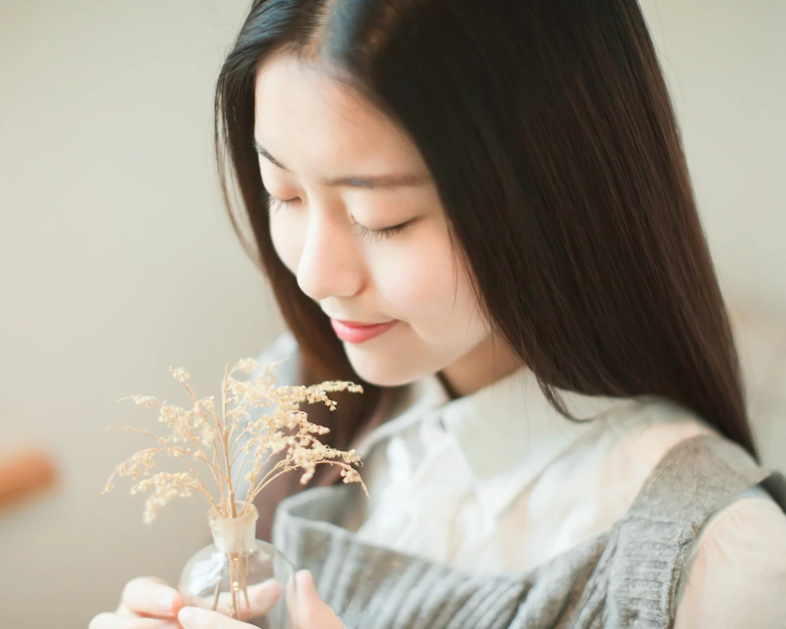 一位长发女性闭眼手捧干花，画面呈现柔和明亮的肖像氛围。