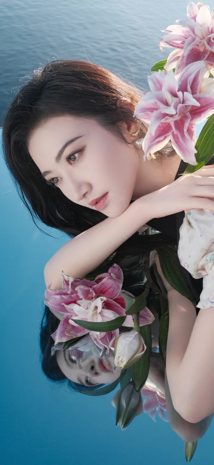 一名女子手捧粉色百合花，倒影映在蓝色水面上。