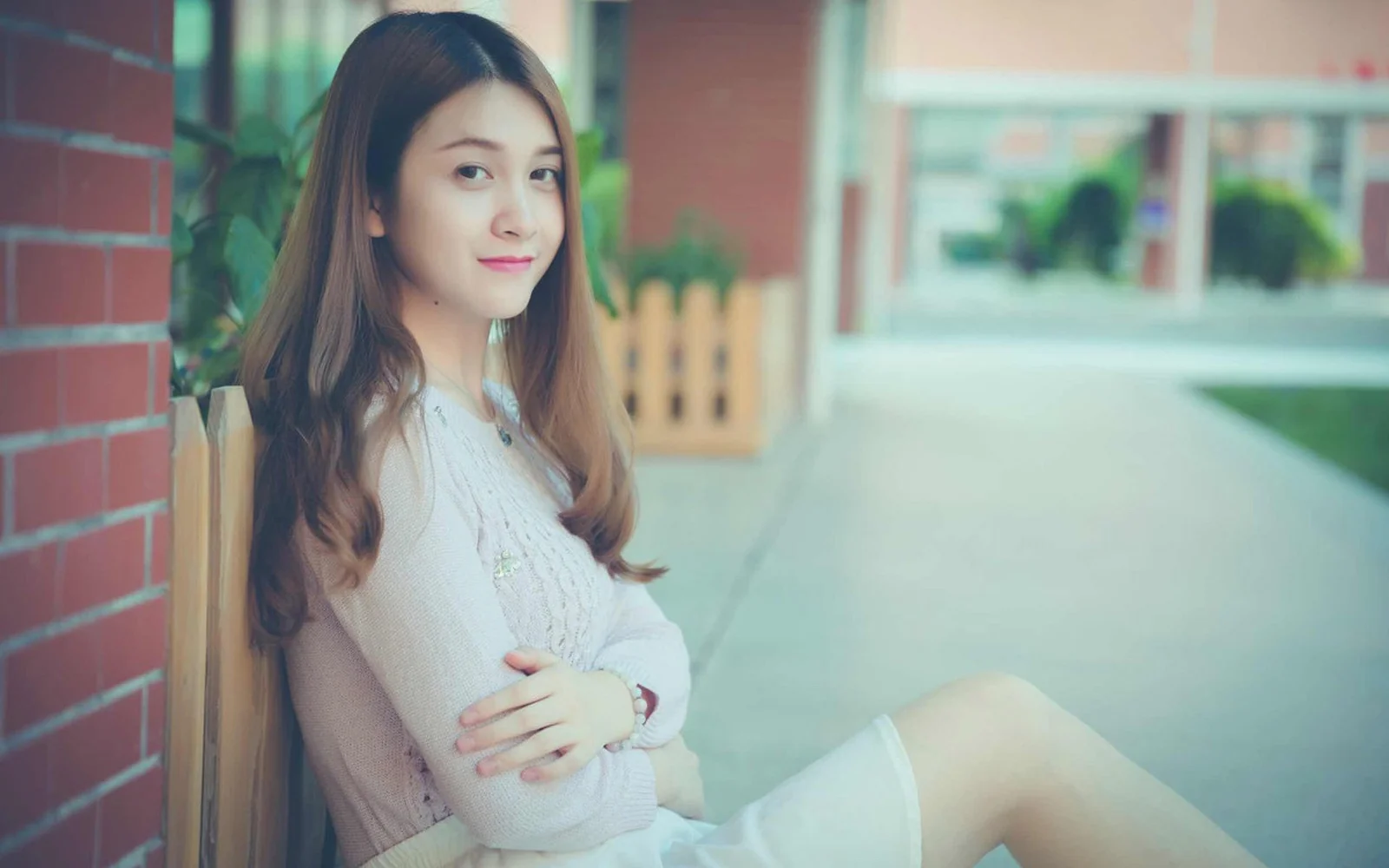一名成年女性坐在磚牆旁，面向鏡頭微笑。