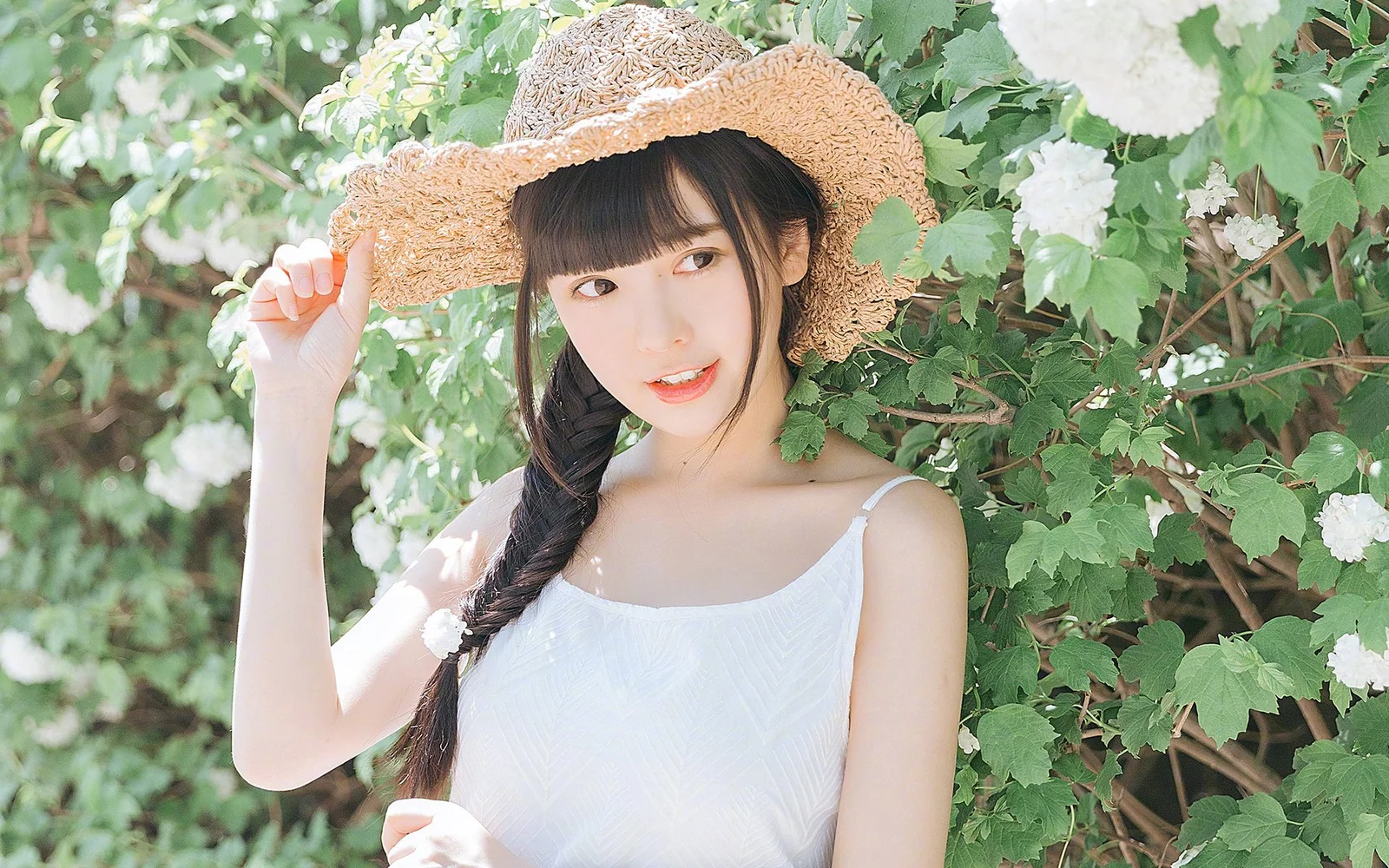 一名戴草帽、留着侧辫的女子站在盛开白花的绿叶间。