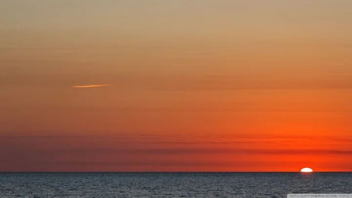 夕阳贴近海平线，橙红色天空映照着平静的海面。