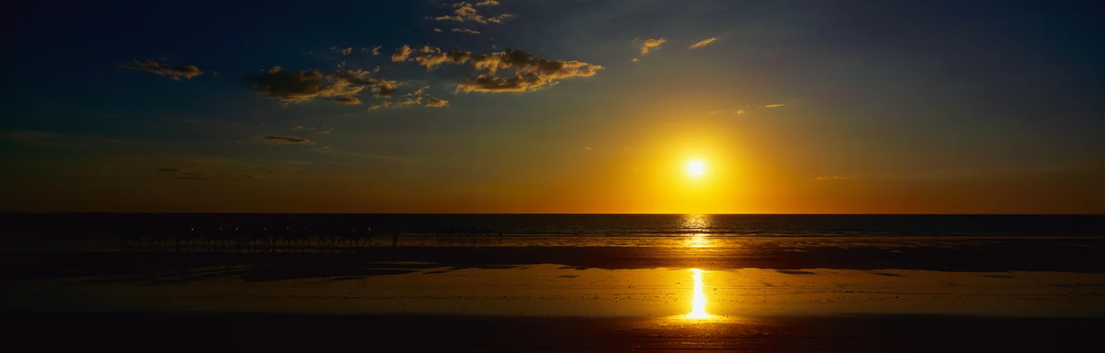 夕阳沉入海平线，金色光芒映照着海面与湿润的沙滩。