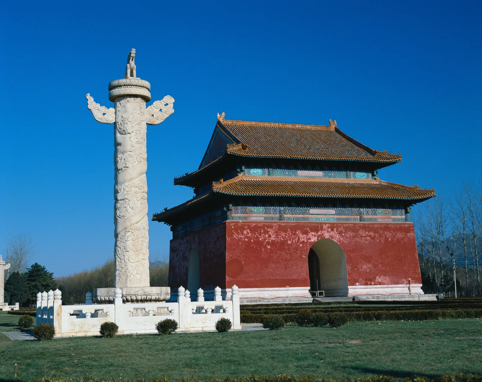 蓝天下，一座红墙古建筑与雕刻石柱坐落在修整整齐的草地旁。