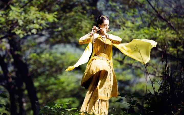 一名身穿黄色服装的成年女子在树林中吹奏长笛。