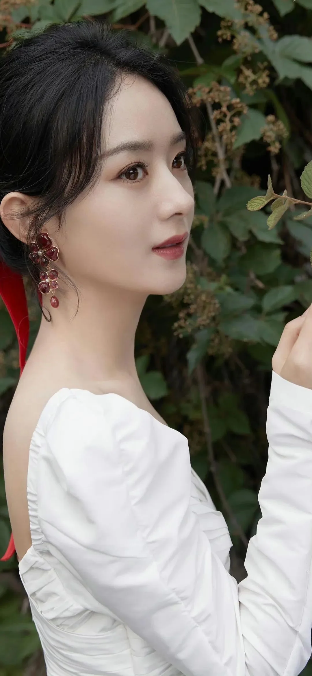 흰색 드레스를 입은 성인 여성이 초록 잎을 배경으로 옆모습을 보이고 있습니다.