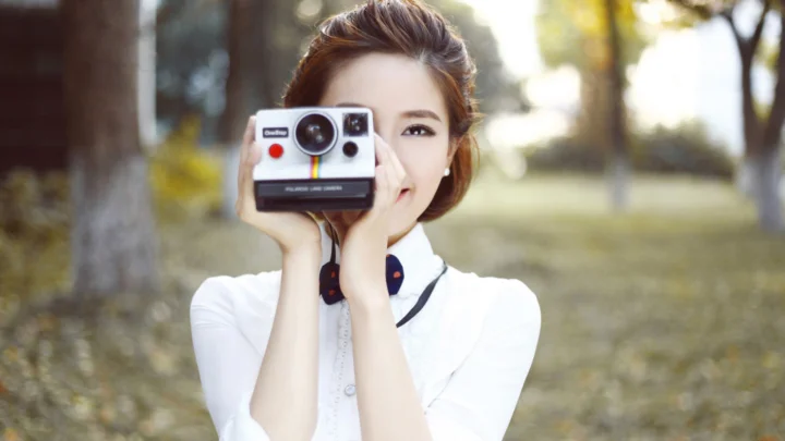 야외 공원에서 한 여성이 즉석카메라를 들고 사진을 찍고 있다.