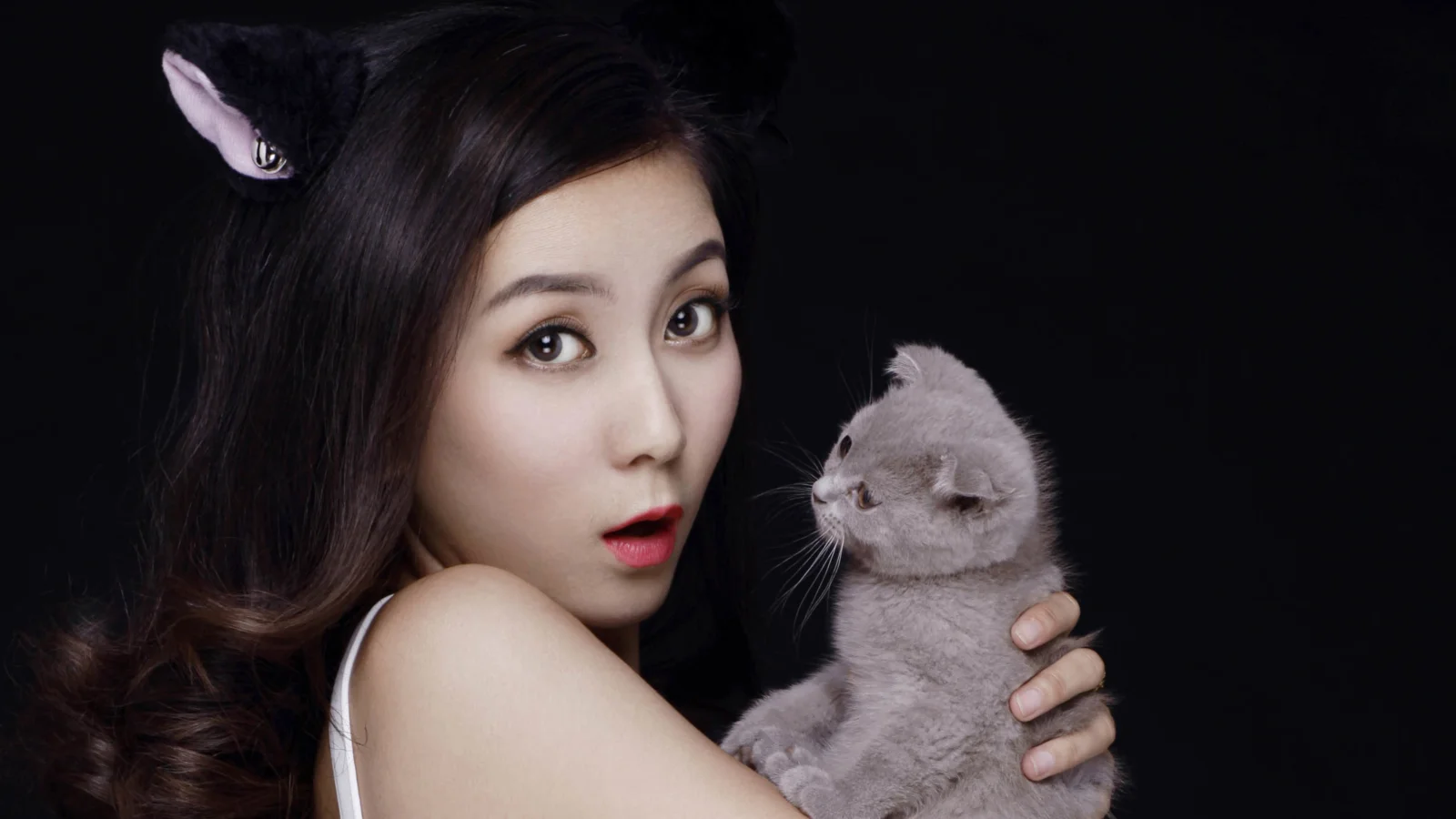 一名女子在黑色背景前抱着一只灰色猫咪。