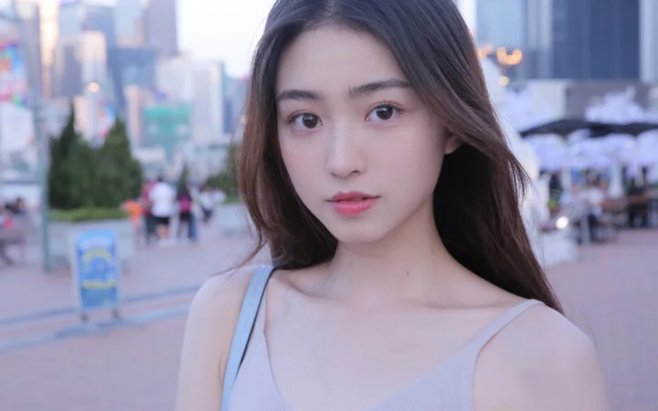 一名长发女性站在城市街头，背景可见模糊的建筑、行人和街道景象。
