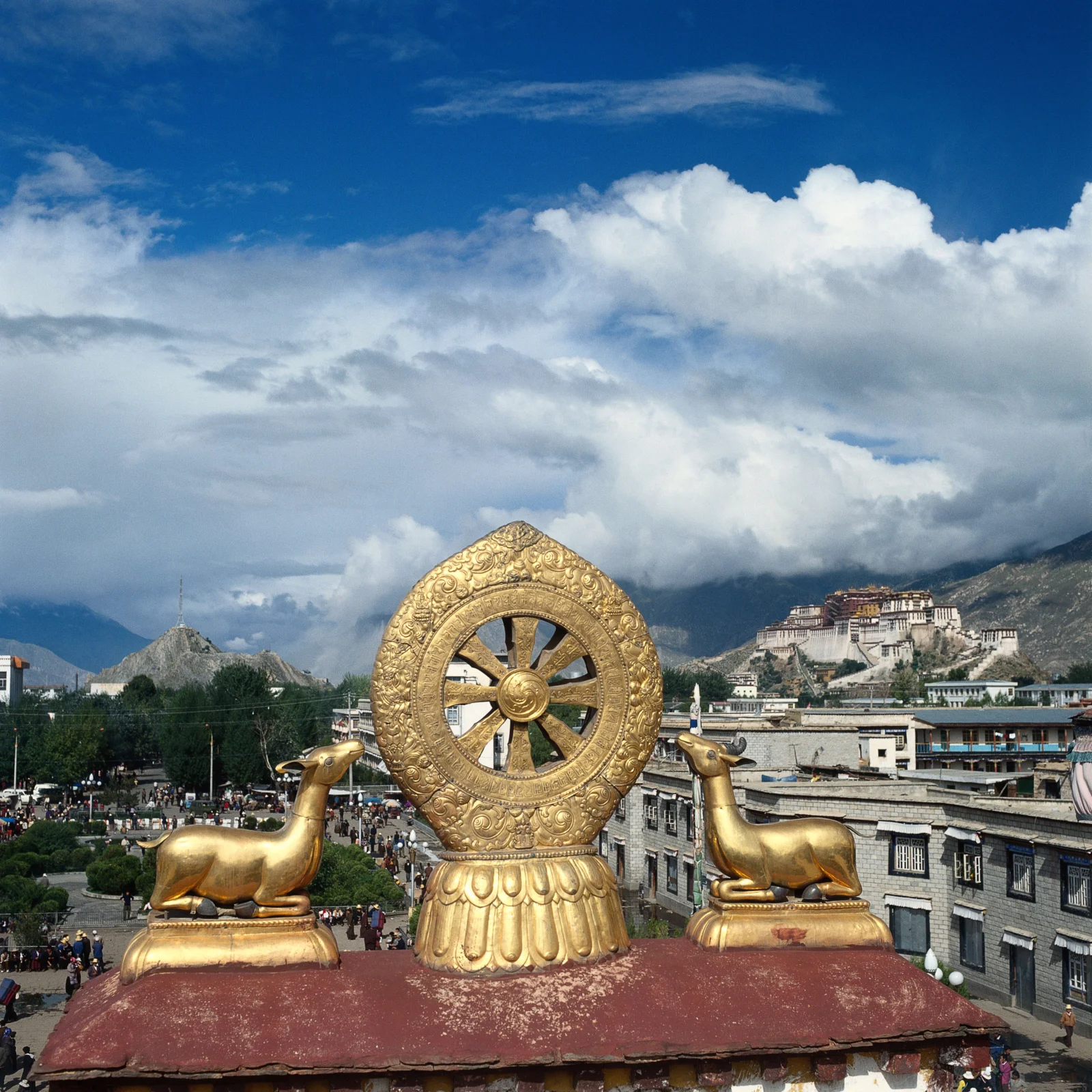 金色佛教法轮和两尊鹿像位于屋顶上方，背景是山间寺院、城镇建筑与壮丽云层。