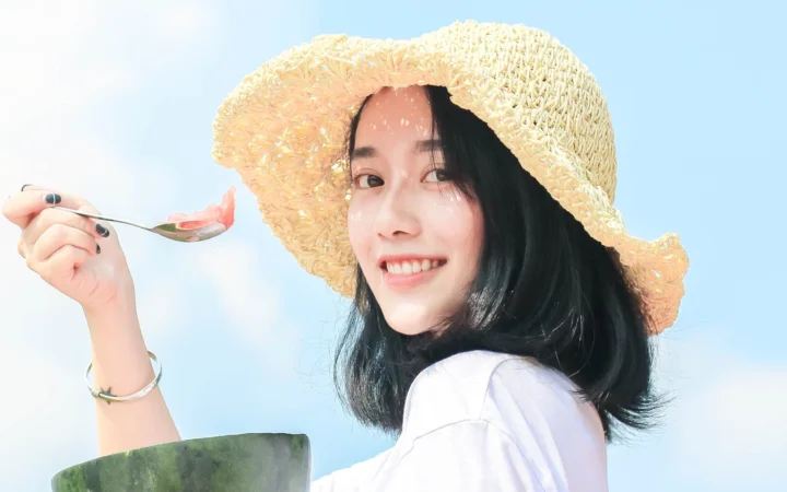 一位戴草帽的女性面带微笑，手持勺子面对镜头。