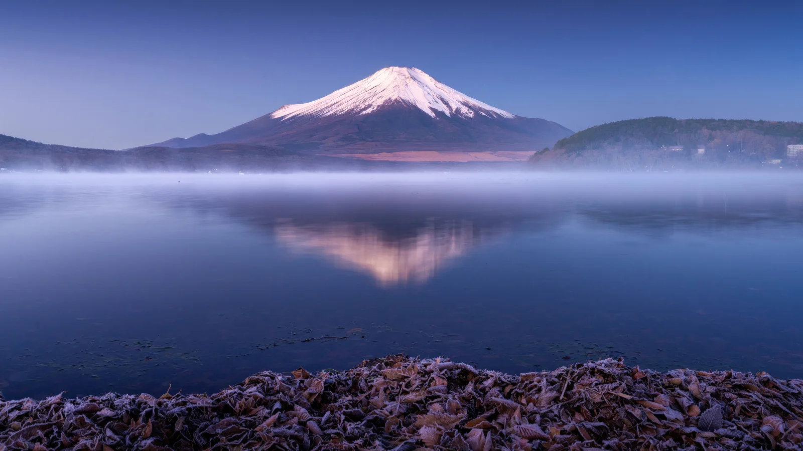 雪を頂いた山が、朝霧に包まれた静かな湖面に映っている。