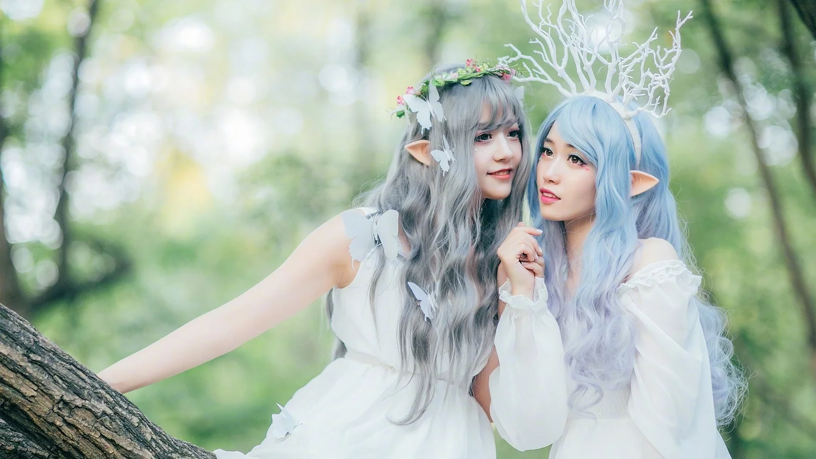 兩名穿著白色服裝、戴著精靈耳朵和鹿角裝飾的女性站在森林中。