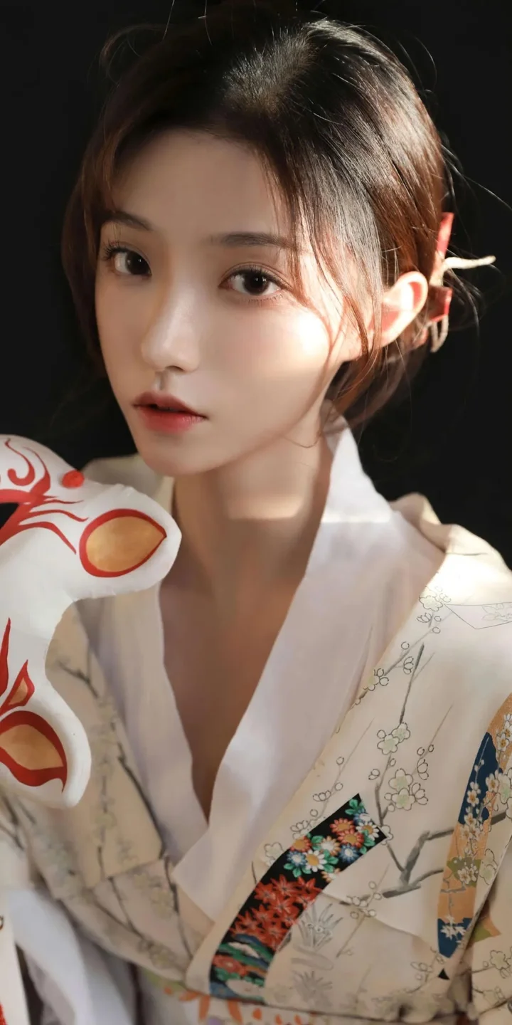 어두운 배경 앞에서 색감 있는 무늬의 흰색 의상을 입은 성인 여성이 카메라를 바라보고 있다.