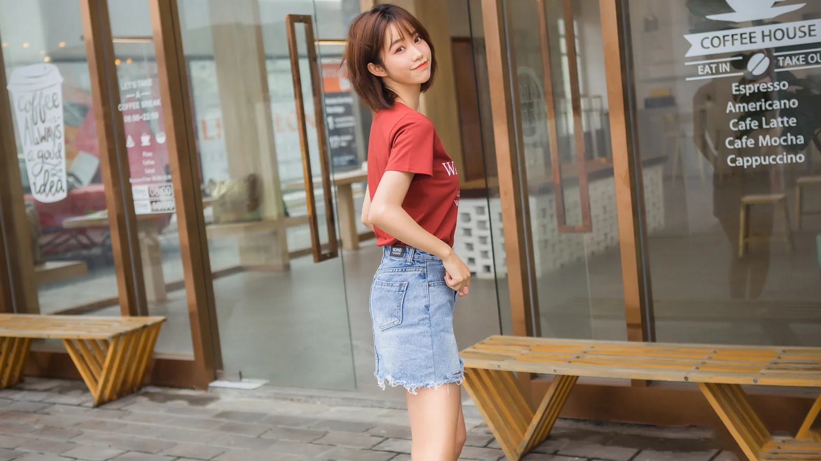 一名成年女子站在咖啡馆玻璃门前，身后可见木质长椅和咖啡店标识。