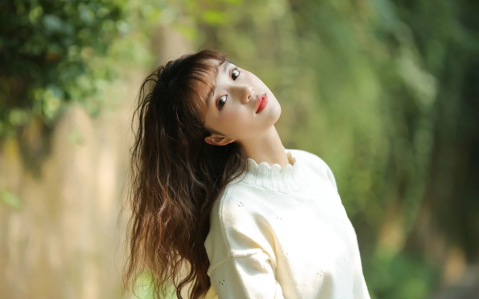 一名身穿白色针织衫的女子站在柔和绿意环绕的森林中。