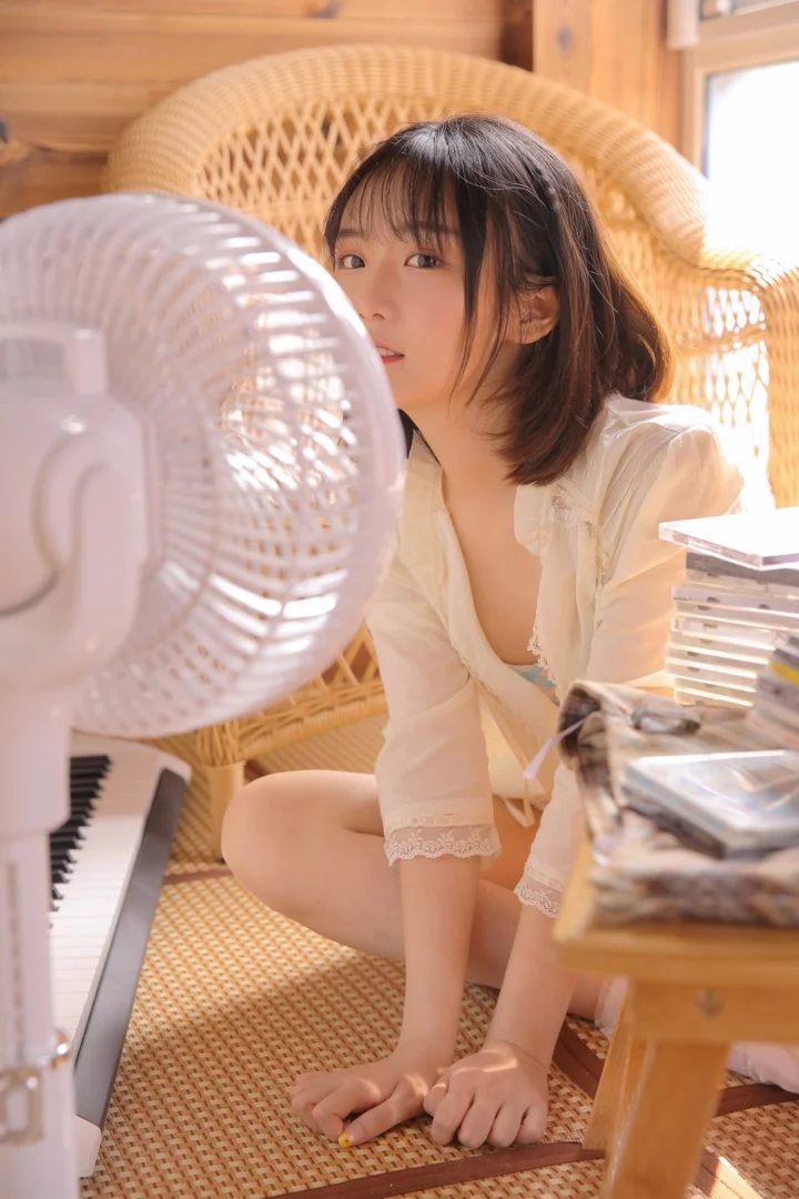 一位女性坐在藤椅上，身旁有电风扇和电子琴，阳光从窗边照入室内。