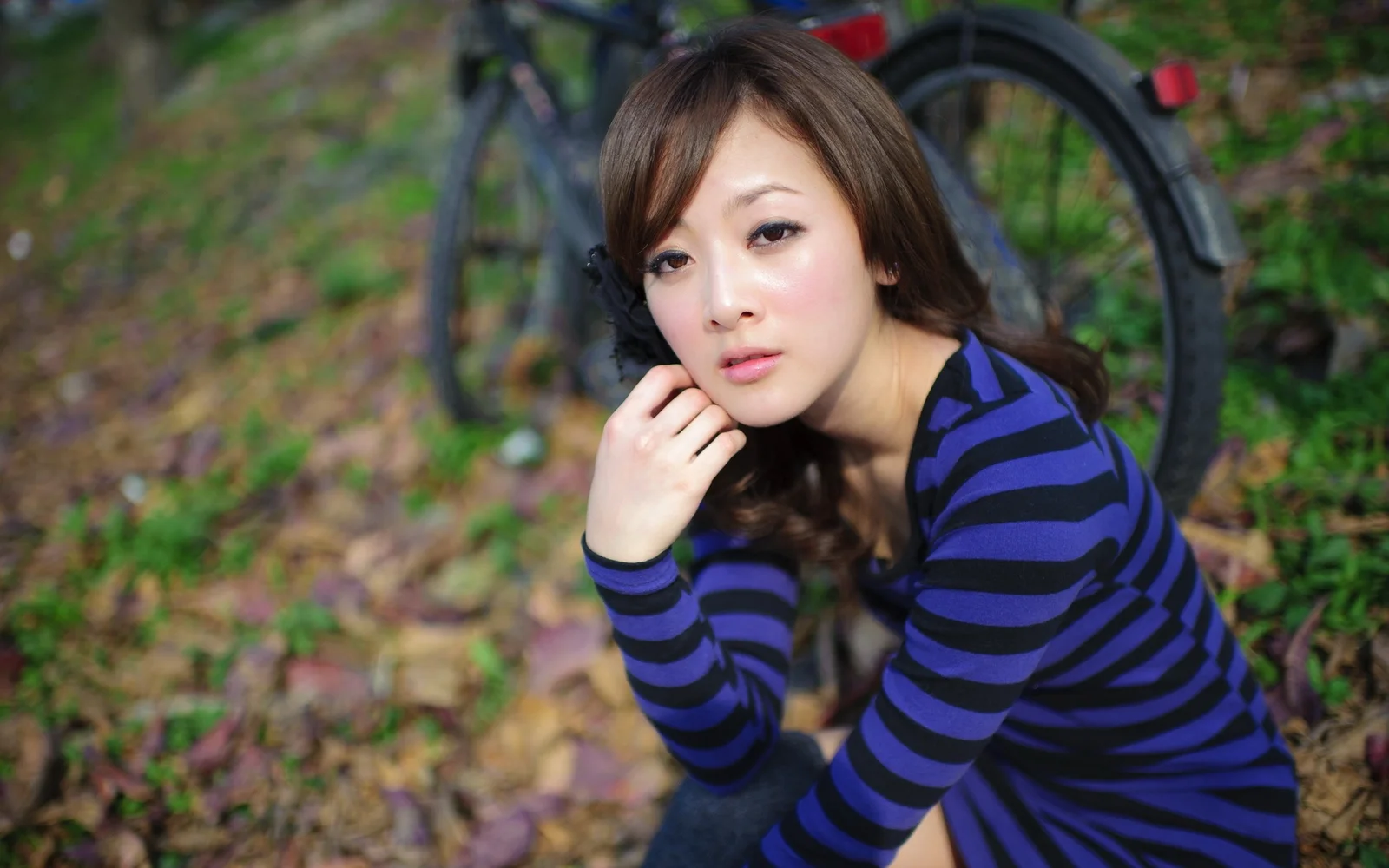 一名身穿蓝黑条纹上衣的成年女性在户外自行车旁看向镜头。