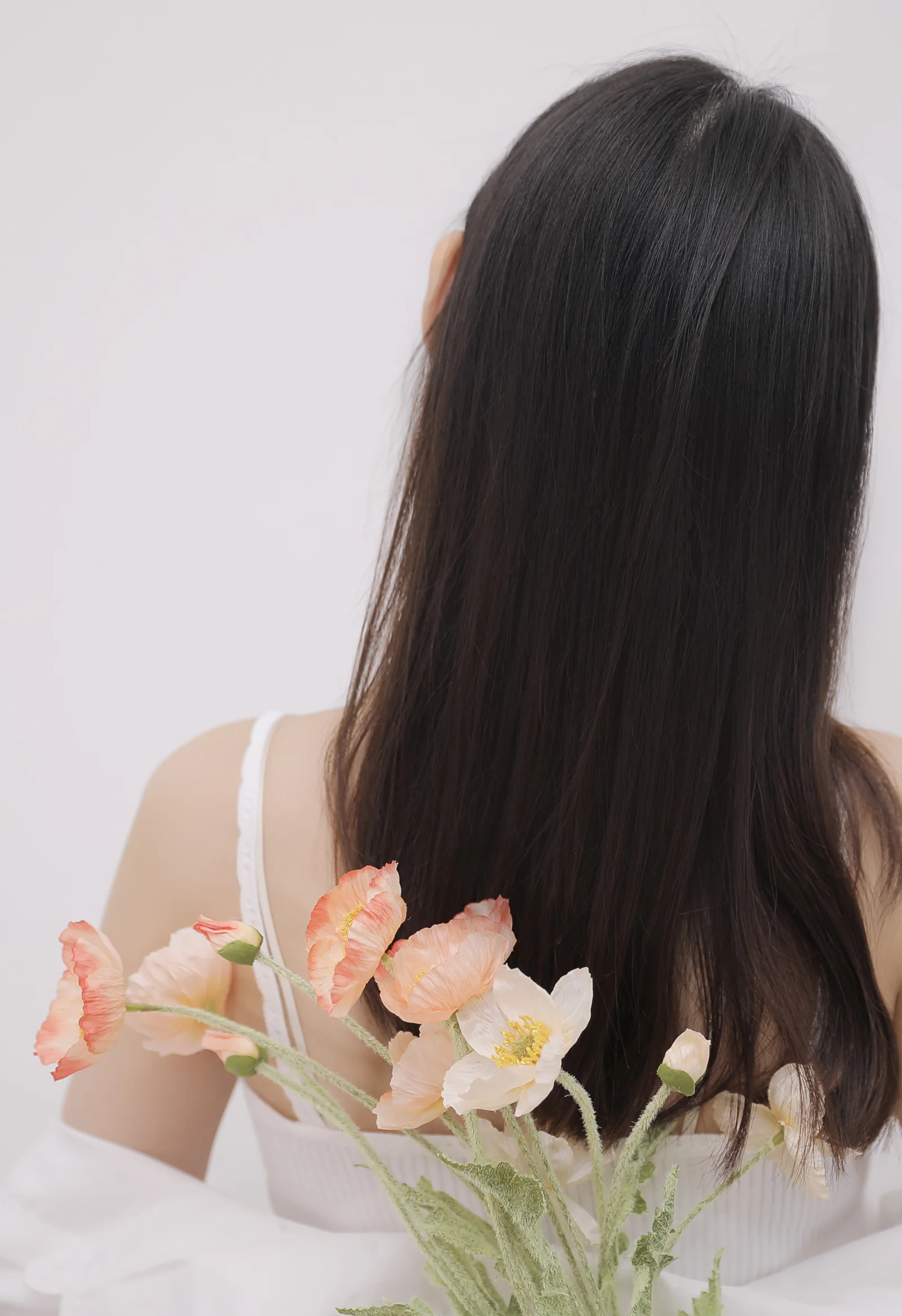 長い髪の人物が背を向けて座り、手前に淡い色の花が添えられています。