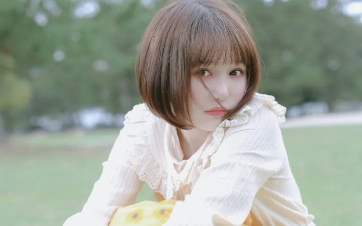 一名短发女子身穿白色上衣，在户外草地前看向镜头。